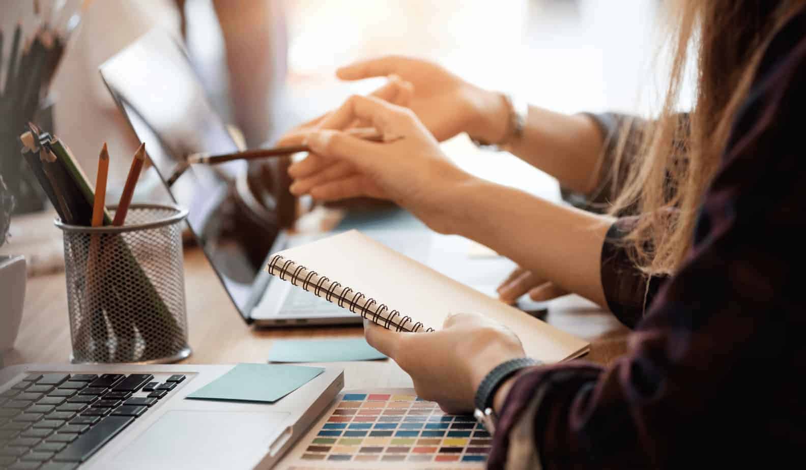 business professionals pointing at screen of laptop while holding a note pad