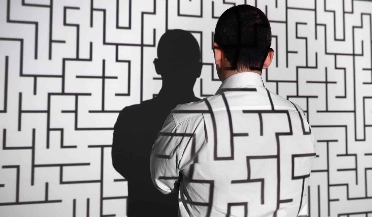 Business man standing facing projector screen with maze on his back