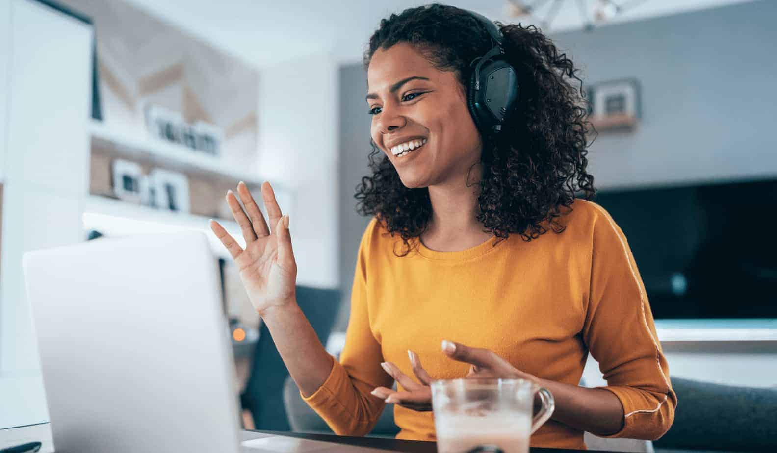 women working at home with headset on waving at computer