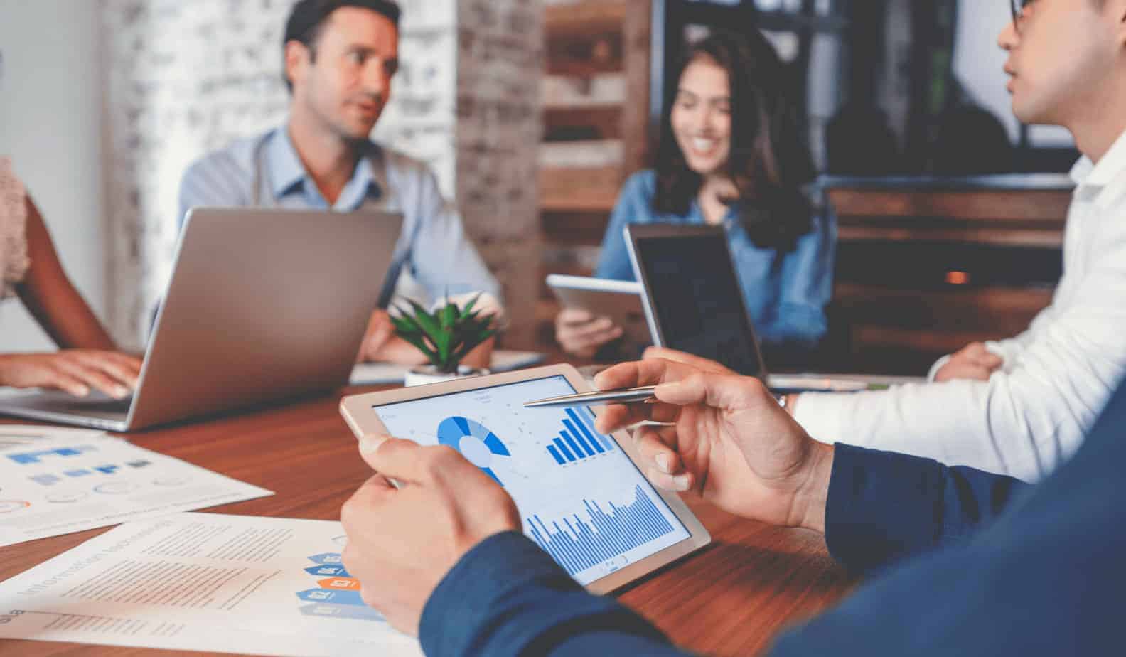 Group of business professionals in meeting room on tablets and laptops