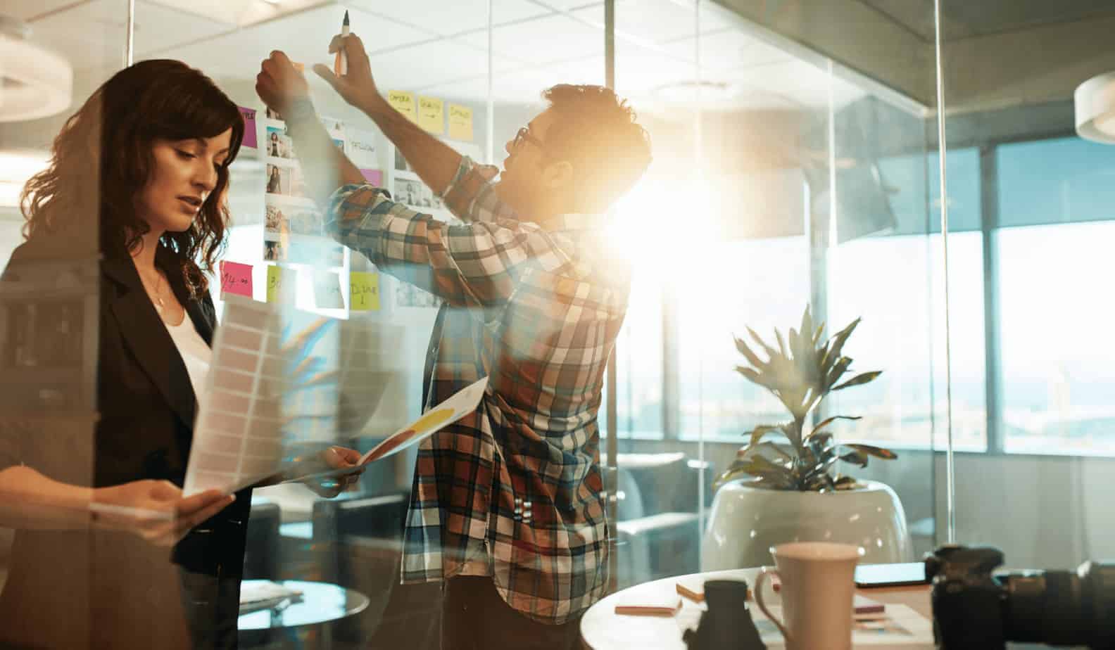 Business coworkers in meeting room hanging sticky notes and pictures on glass window