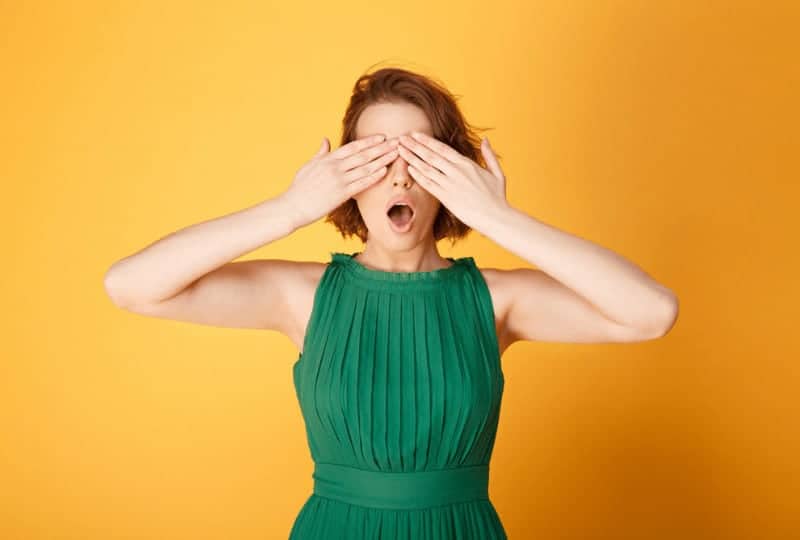 girl covering her eyes in front of a yellow background