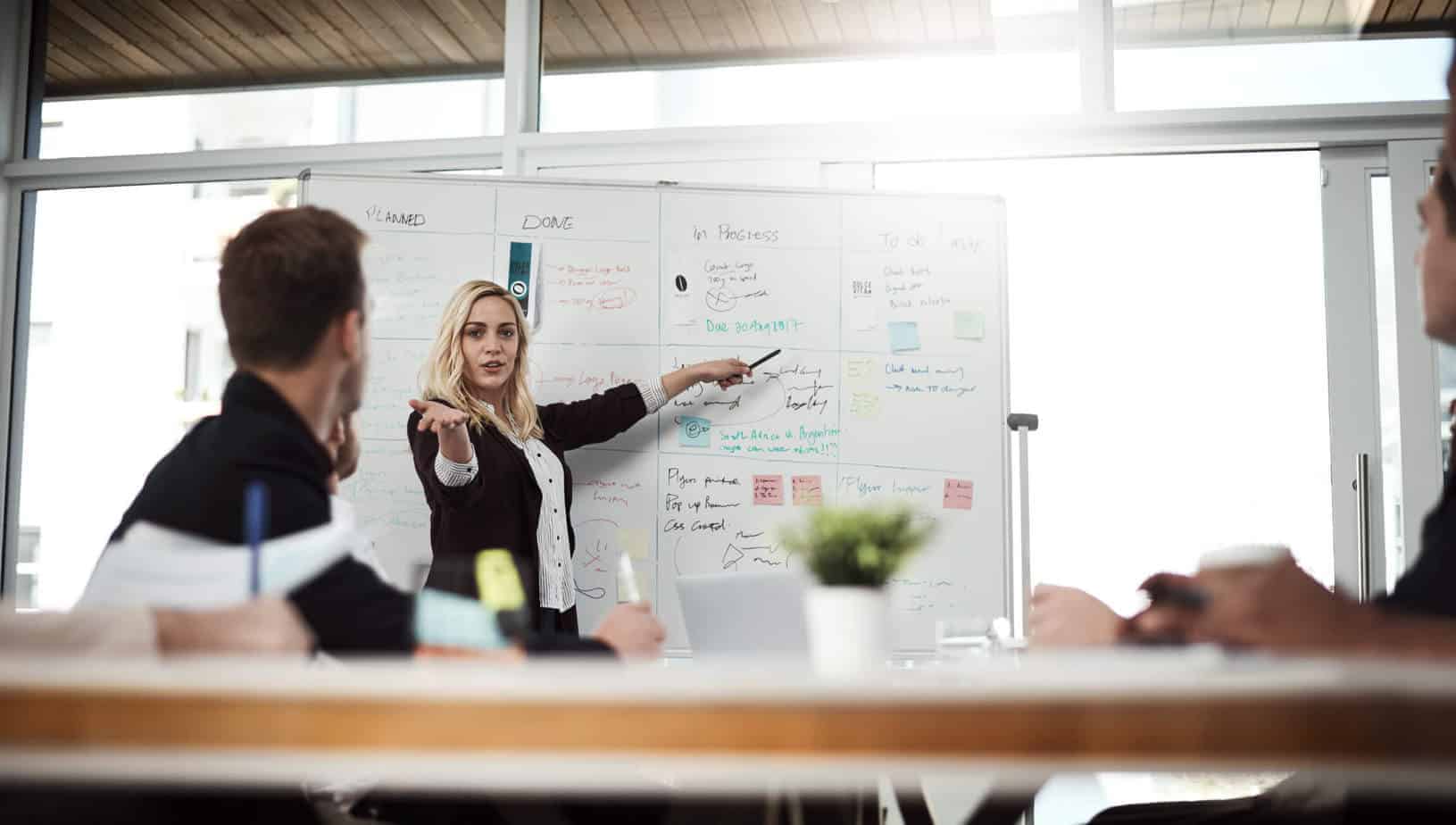 woman pointed to a whiteboard leading a meeting