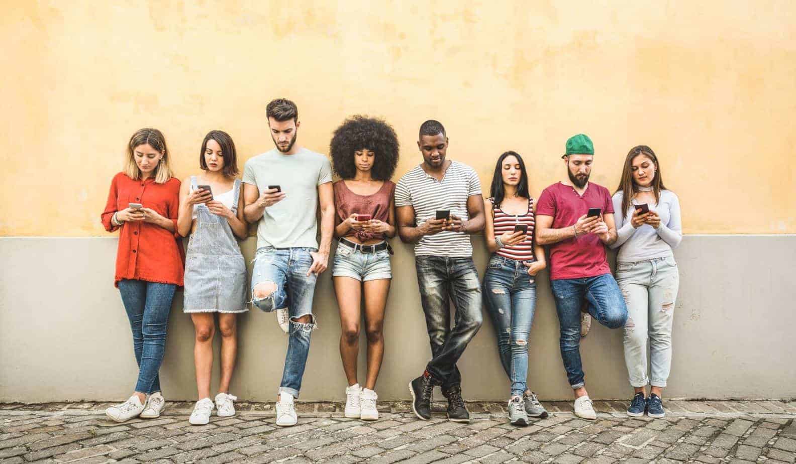 group of eight people leaning up on the wall looking at their phones