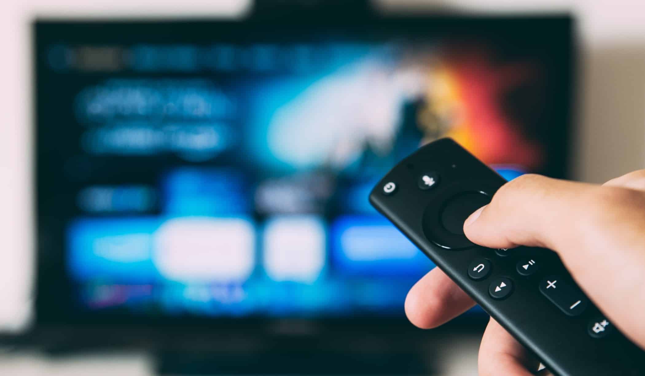 blurry background of a tv screen, focus on a hand holding a black remote