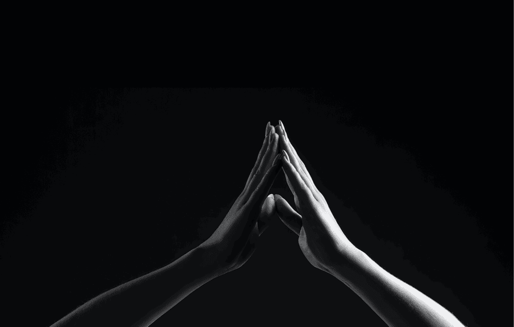 black and white hands in a "prayer" placement in front of a black image