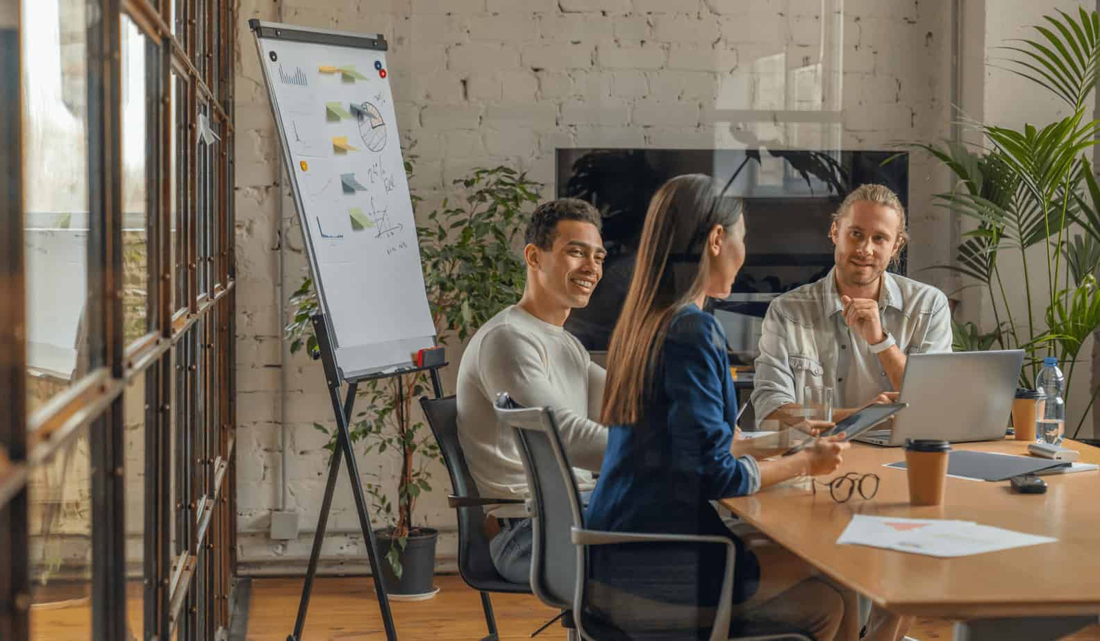 Group of young business professionals in meeting room with charts and graphs on whiteboard.