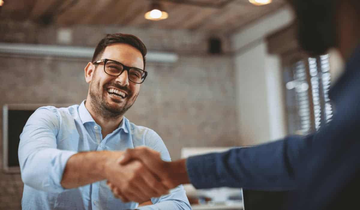 two men shaking hands, the man in focus is smiling widely