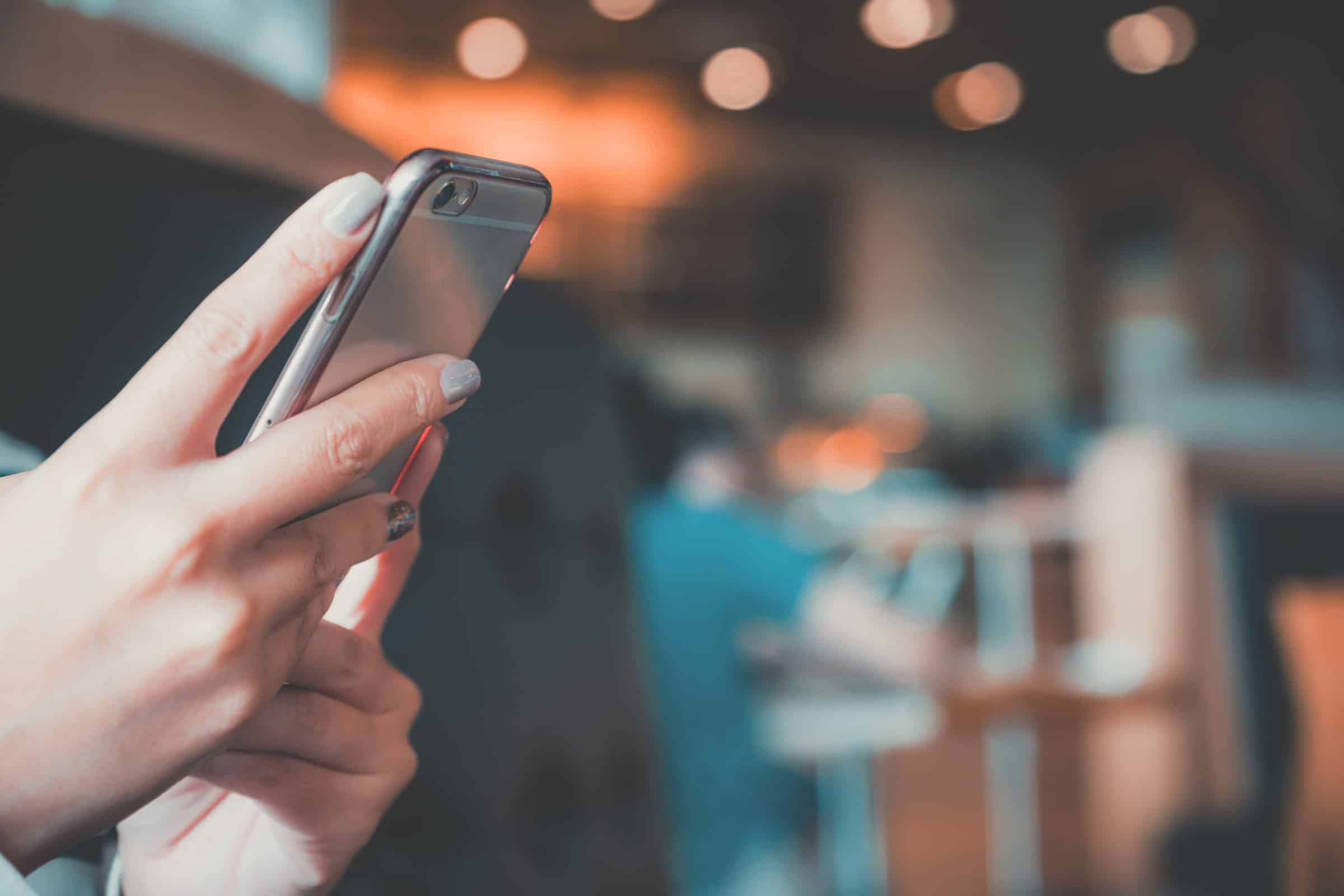 Closeup image of a woman's hands holding , using and looking at smart phone in cafe with blur background