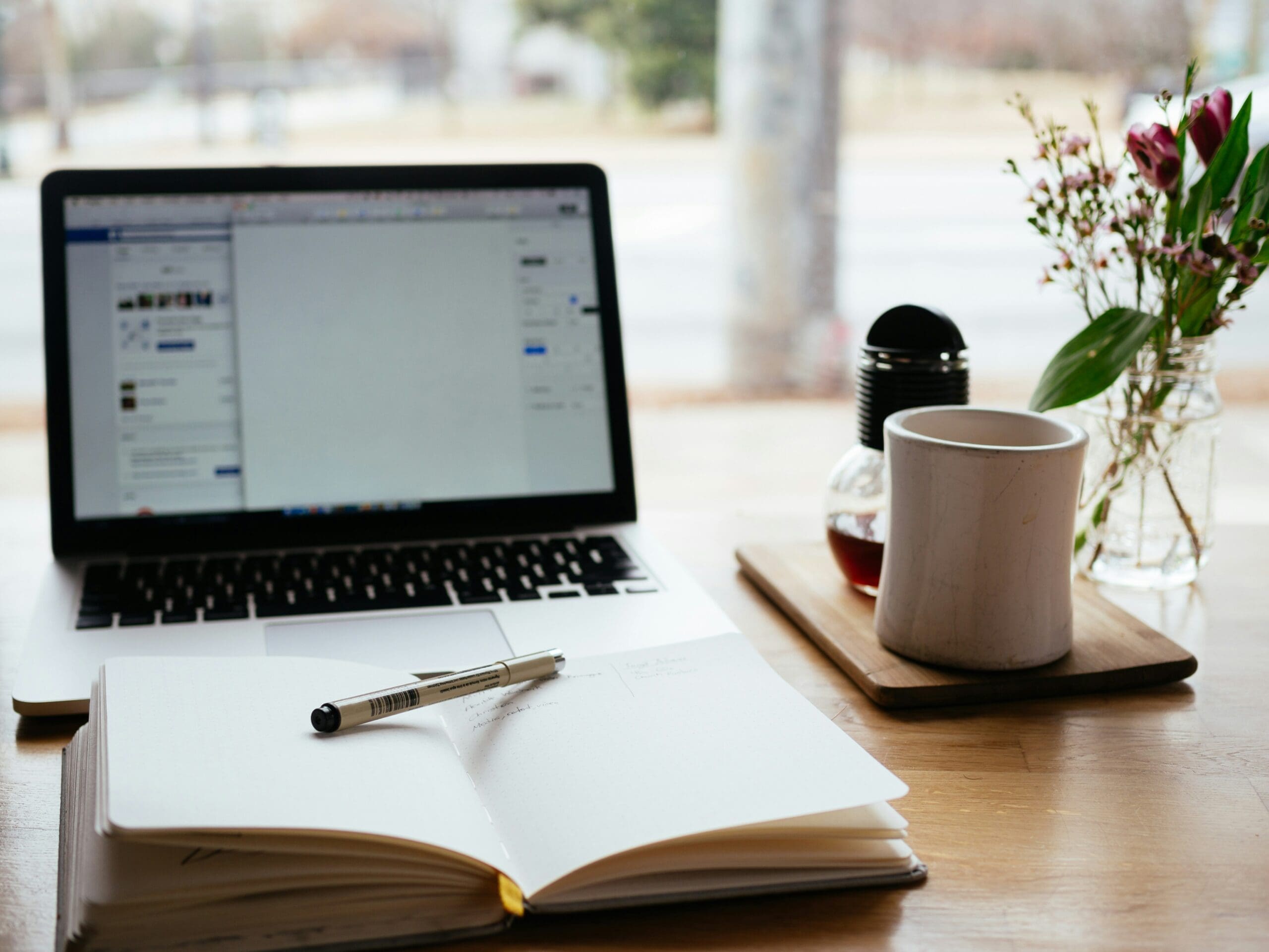 Laptop computer open with a notebook and coffee cup next to it