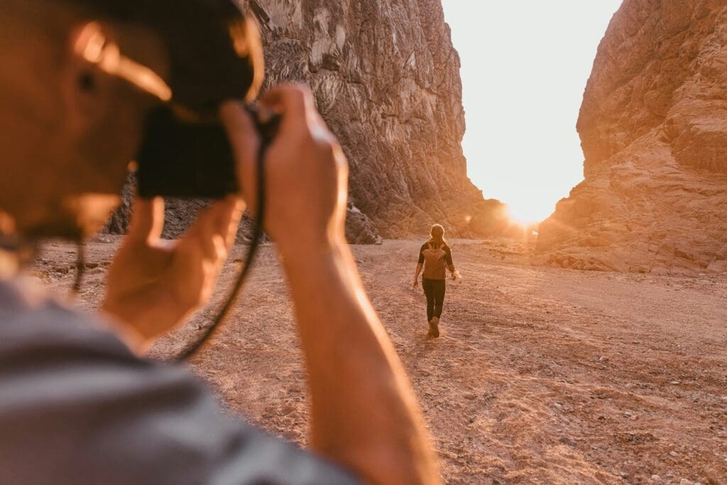 Person with a camera taking a photo of someone else in a desert